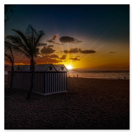 Ein stimmungsvoller Sonnenuntergang über dem Meer an einem Sandstrand. Im Vordergrund stehen Palmen und eine gestreifte Strandhütte als Silhouette, während die Sonne goldene Strahlen wirft.