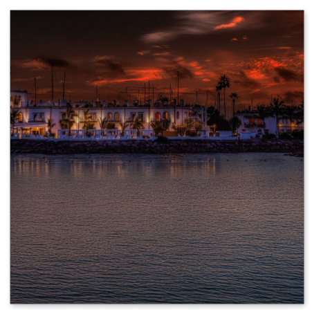  Eine nächtliche Ansicht des beleuchteten Hafens von Puerto de Mogán auf Gran Canaria. Die weißen Gebäude spiegeln sich im ruhigen Wasser des Hafenbeckens unter einem dramatisch rot glühenden Abendhimmel.