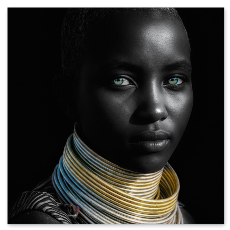 Nahaufnahme einer afrikanischen Frau mit kurzen Haaren und strahlenden, blau-grünen Augen, die breite, traditionelle Halsringe in Silber und Gold vor einem dunklen Hintergrund trägt.