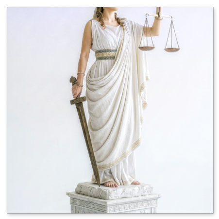 Eine lebensechte Justitia-Figur mit weißer Augenbinde und goldenem Lorbeerkranz steht barfuß auf einem verzierten Sockel mit römischer Inschrift. In der rechten Hand stützt sie ein antikes Schwert auf den Boden, in der erhobenen linken Hand hält sie eine Waagschale.
