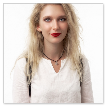 Porträt einer jungen Frau mit blonden, gewellten Haaren und blauen Augen vor rein weißem Hintergrund. Sie trägt eine weiße Leinenbluse, auffallend roten Lippenstift und eine Halskette mit einem kleinen Schneeflocken-Anhänger.